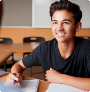 a young person sits at a desk studying and looks up and smiles at another person