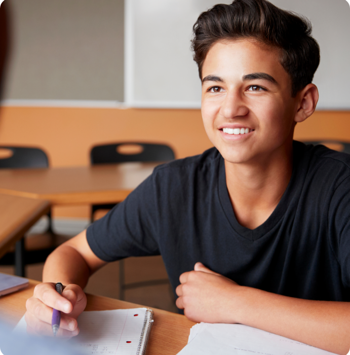 a young person sits at a desk studying and looks up and smiles at another person