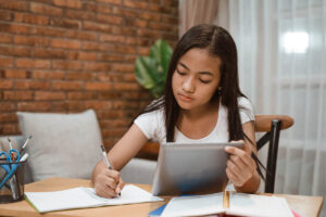 a teen looks at a tablet and writes on a piece of paper while learning about OCD