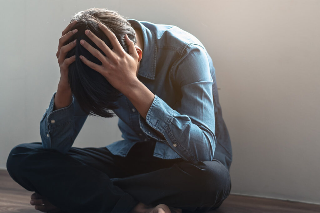 person sitting with head in hands contemplating the question is self-harm a mental health issue
